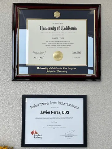 Dr. Perez's University of California, Los Angeles School of Dentistry diploma and an Implant Pathway certificate, framed on the office wall.